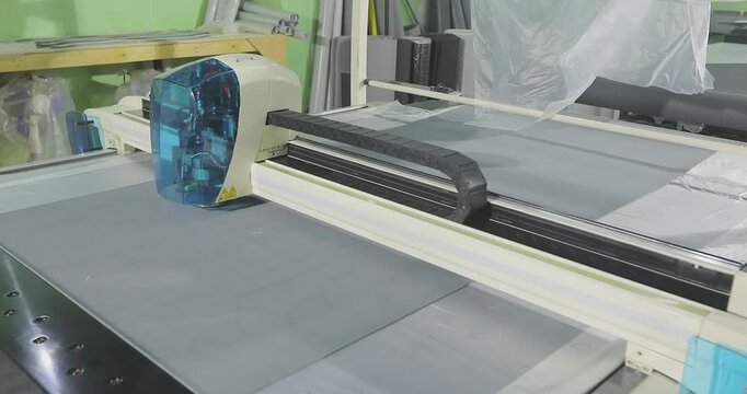 Automated cutting of grey upholstery fabric on a CNC plotter. Fabric cutting process on a CNC machine in a modern production workshop. Garment or furniture factory.