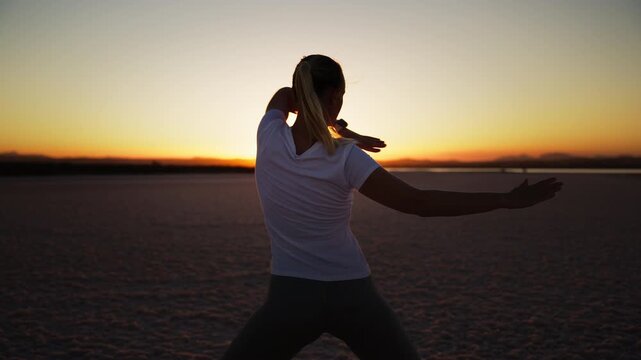 Silhouette of a woman practicing tai chi and meditation exercises at sunset, finding balance, wellness, and inner peace in a stunning natural landscape with lens flare