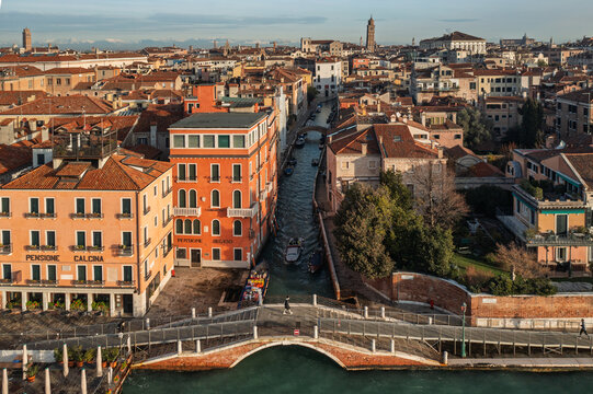 Aerial view of the historic buildings and canals, featuring the Pensione Calcina, a stone bridge, and boats navigating the waterway in Venice, Veneto, Italy.