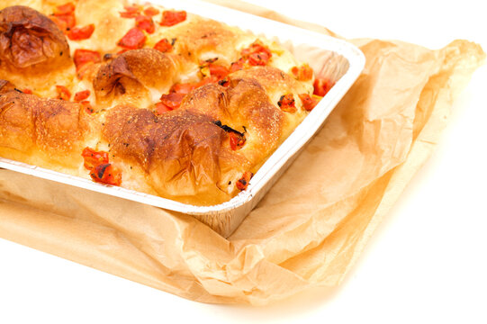 Freshly baked Italian focaccia bread with tomatoes in an aluminum tray isolated on white background
