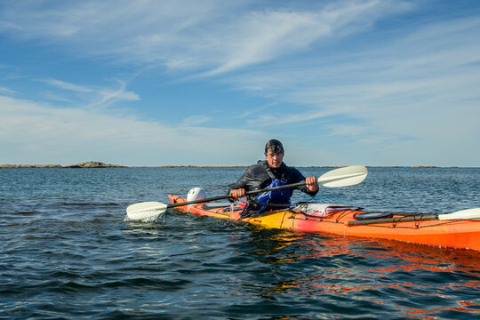 Sea kayaker paddles an orange kayak across open water under sweeping cirrus clouds with copy space on Georgian Bay, Ontario, Canada