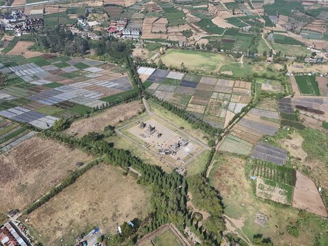 Aerial view of Arjuna Temple surrounded by agricultural fields and lush greenery in Kecamatan Batur, Jawa Tengah, Indonesia.