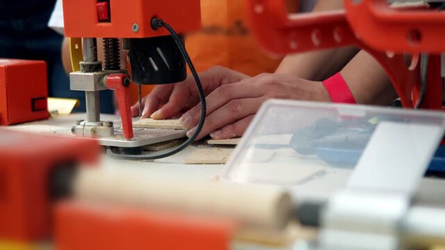 Artisan operates compact electric milling machine to pierce light plywood during creative crafting session. Wood dust scatters across work table as metal drill bit penetrates solid material.