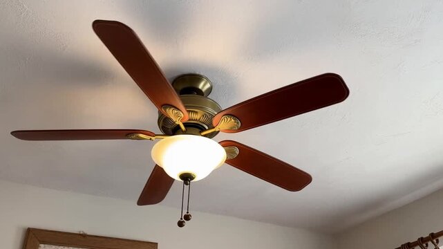 Static shot of ceiling fan spinning overhead in residential living room with illuminated light fixture and pull chains