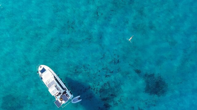 Aerial view of Blue Lagoon with a boat and a person swimming in clear turquoise water, Malta.