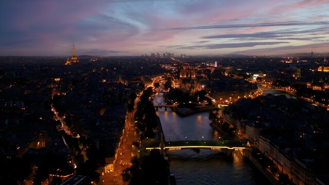Aerial view of the Eiffel Tower and Notre-Dame Cathedral illuminated at dusk over the Seine River in Paris, Ile-de-France, France.
