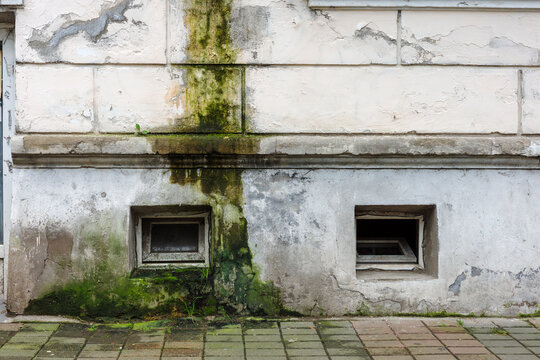 Peeling facade with damp streak, mold, cracked plaster, basement windows and water damage, neglected building maintenance, leakage and renovation need