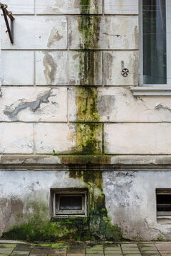 Moisture stain, algae and deteriorated facade with cracked plaster, peeling paint and vertical water intrusion showing persistent exterior leakage