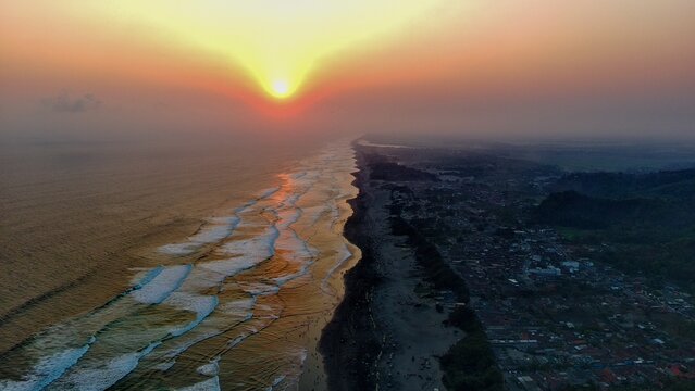 Aerial view of Parangtritis Beach at sunset with golden light reflecting on the waves and the coastline of Kretek, Special Region of Yogyakarta, Indonesia.