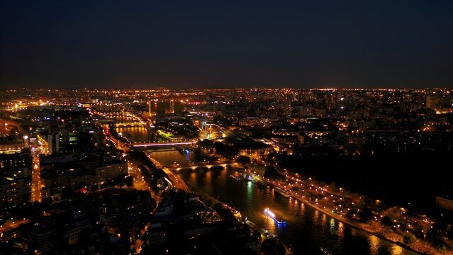 Aerial view of the illuminated Paris cityscape at night, featuring the Seine river, glowing bridges, and dense urban lights stretching to the horizon in Paris, Ile-de-France, France.