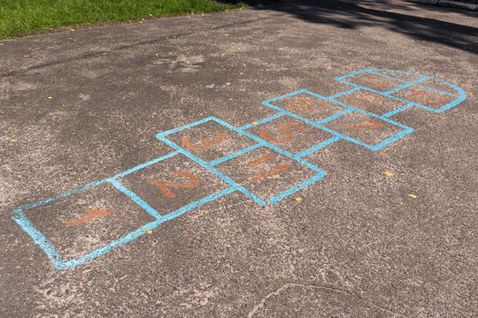 Painted hopscotch game grid with numbers on asphalt close-up. Colorful blue and orange numbered hopscotch grid drawn on pavement surface