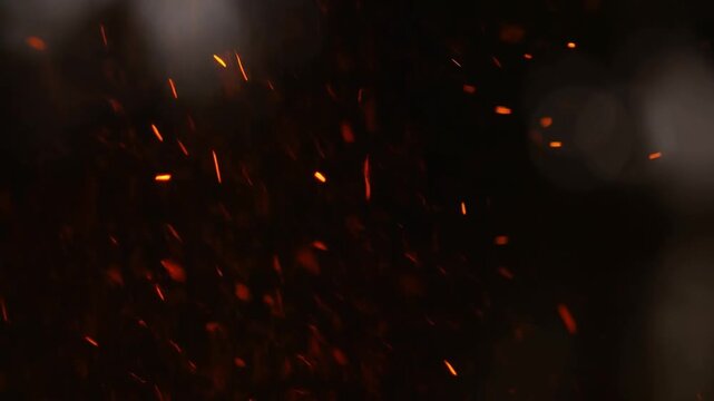 Slow motion tracking shot of glowing embers rising from fire pit in dark smoky environment