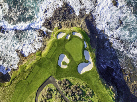 Aerial view of the 7th hole at Pebble Beach Golf Links, featuring a green surrounded by sand bunkers and rugged cliffs overlooking the Pacific Ocean, Pebble Beach, CA, United States.