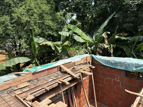 House construction site in Kerala, India, showing a residential building under construction with concrete structures, construction materials, and a developing house structure. The image represents res
