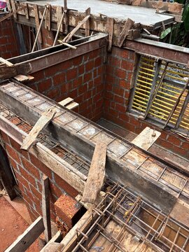 House construction site in Kerala, India, showing a residential building under construction with concrete structures, construction materials, and a developing house structure. The image represents res