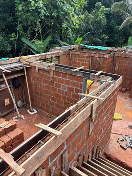 House construction site in Kerala, India, showing a residential building under construction with concrete structures, construction materials, and a developing house structure. The image represents res