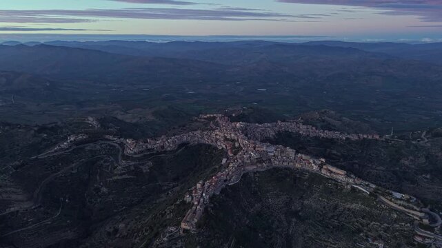 Aerial view of the star-shaped town of Centuripe nestled on a mountain ridge with surrounding hills and twilight sky in Centuripe, Sicily, Italy.