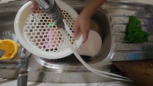 POV view of a man washing dirty plates in a kitchen sink. Hands scrubbing dishes under running water during daily household chores. Concept of home routine, cleanliness, and domestic lifestyle.