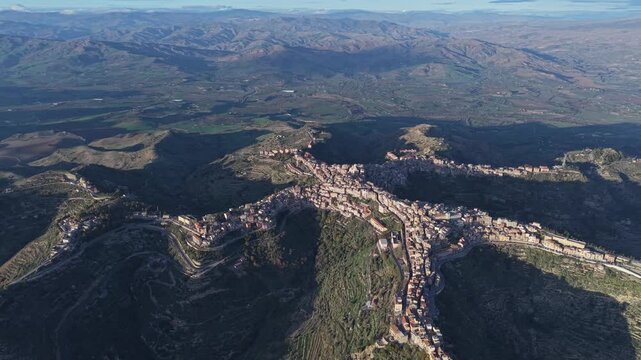 Aerial view of the town of Centuripe, shaped like a human figure, nestled among the rugged hills and valleys of Centuripe, Sicily, Italy.
