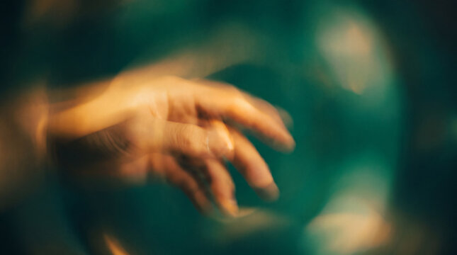 A conceptual artistic shot featuring a human hand captured with intentional motion blur, surrounded by warm golden light against a dark teal background.