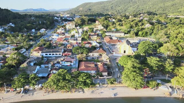 Aerial drone top view of the historic Nossa Senhora das Necessidades church plaza and colonial streets in Santo Antonio de Lisboa village, Florianopolis, Santa Catarina, Brazil, during sunny golden ho