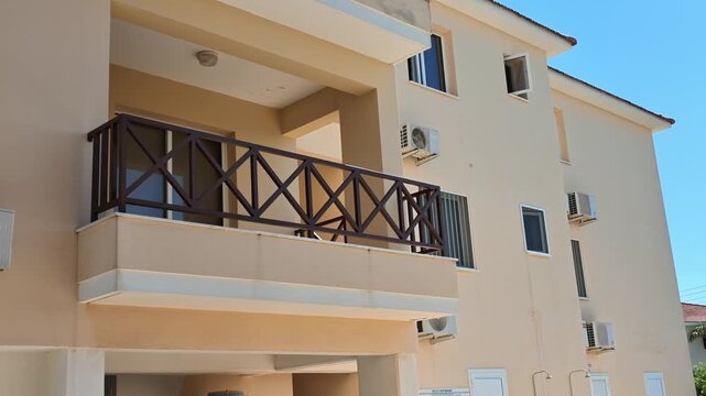 Apartment building exterior with a balcony, dark railing, windows and air conditioning units under a clear blue sky