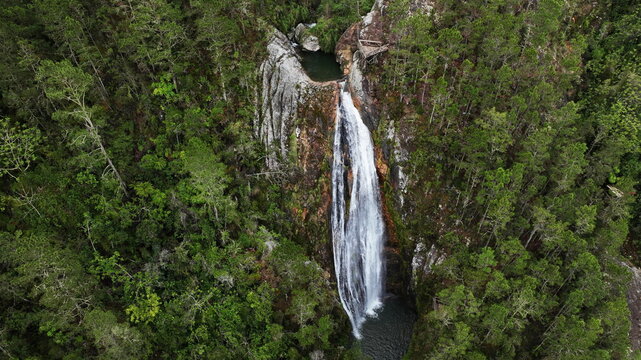 Aerial view of Salto de Aguas Blancas waterfall cascading down rocky cliffs surrounded by dense pine forests in the mountains of Constanza, La Vega Province, Dominican Republic.