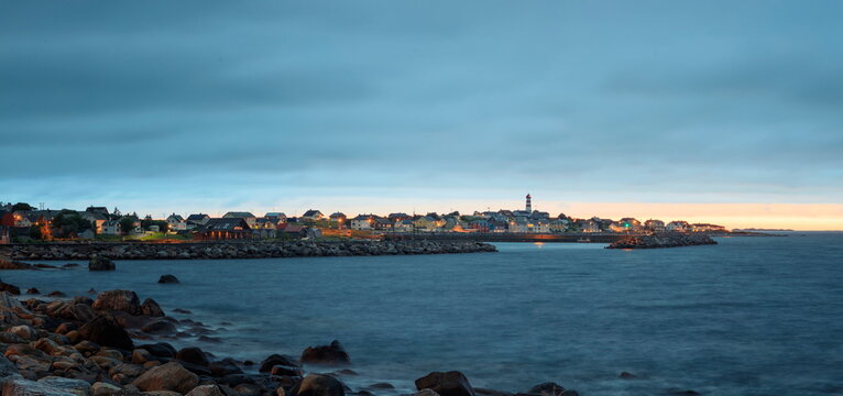 Alnes, Norway - 26.06.2024: Coastal village with lighthouse and rocky shore under a deep blue twilight sky with long exposure water