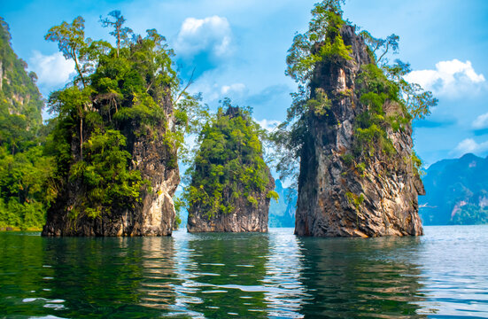 Cheow Lan Lake in Thailand. Impressive limestone cliffs rising above the calm waters of a tropical lake, surrounded by lush rainforests under a brilliant blue sky.
