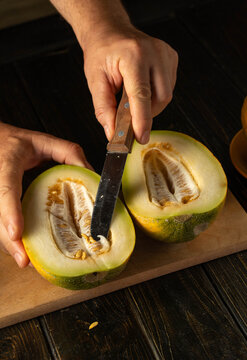 Hands skillfully slice through the smooth skin of a fresh melon, exposing the creamy, seed-filled center. The warm kitchen atmosphere enhances the moment of preparation and enjoyment