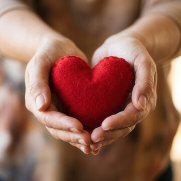 Hands holding a red heart symbol representing love care and compassion with a soft focus background