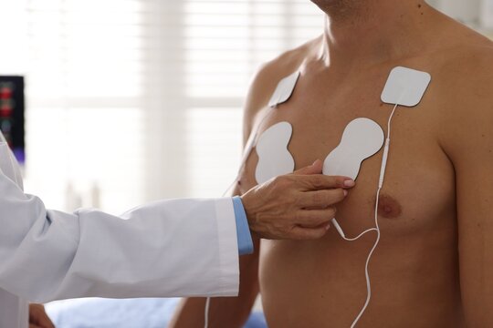 Doctor attaching ECG electrodes to patient's chest in clinic, closeup