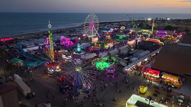 CALIFORNIA - 9.2.2026 - Incredible aerial footage circling the Ventura County Fair's amusement park rides including a Ferris wheel and log flume ride, resting on the beach at sunset.