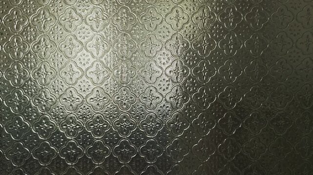 Sunlight or artificial light creating subtle bokeh and distorted reflections behind a translucent, patterned privacy glass panel