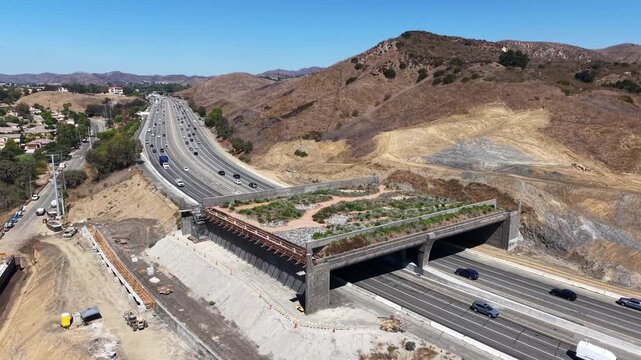CALIFORNIA - 9.22.2026 - Beautiful leftward aerial view of the Wallis Annenberg Wildlife Crossing, still under construction, as Highway 101 traffic passes beneath it.