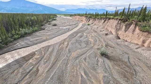 ALASKA - 9.3.2026 - Amazing aerial footage following a bush pilot flying over outwash in Alaska, surrounded by thick green forests.