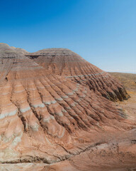 Layered eroded hills form striking horizontal ridges beneath a clear blue sky, creating an arid geological landscape ideal for travel, geology and desert design themes. © UQink