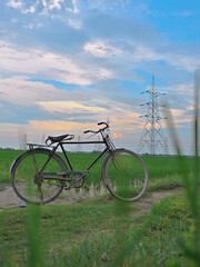 Bicycle stands beside a rural road with power pylons crossing green fields beneath a soft evening sky, blending cycling, travel, agriculture and energy infrastructure themes. © UQink