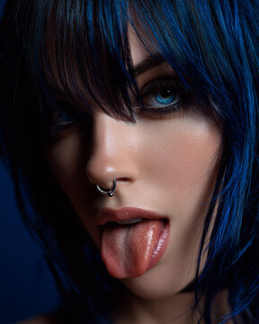 Young woman with blue hair and septum piercing sticking out tongue