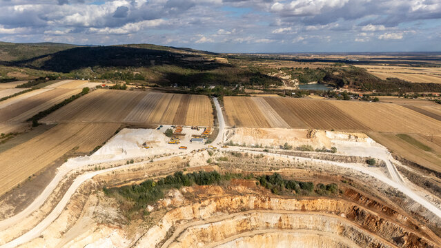 Aerial view of the open-pit quarry in Besenovo surrounded by agricultural fields and rolling hills under a cloudy sky in Vojvodina, Serbia.