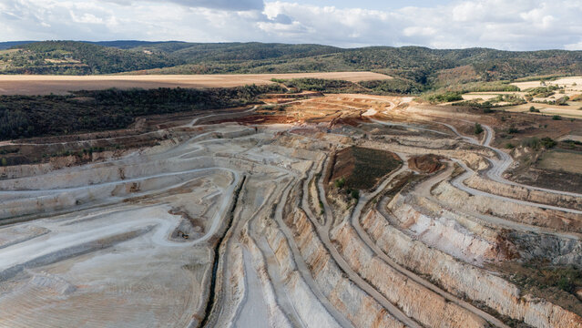 Aerial view of the open-pit quarry in Besenovo, featuring terraced excavation levels, winding access roads, and surrounding hilly landscape under a cloudy sky in Besenovo, Vojvodina, Serbia.