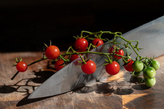 Small cocktail tomatoes hang from a cluster placed over a sharp knife. The large knife is on a wooden cutting board.