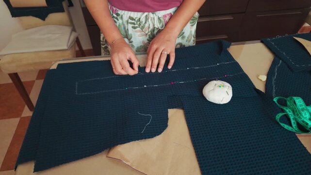 Woman's Hands Precisely Pinning Fabric for Tailoring, Showcasing a Dedicated Crafting Process in a Home Workshop.