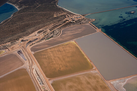 Aerial view of salt evaporation ponds with varying water colors and textures situated along the coastline in Australia.