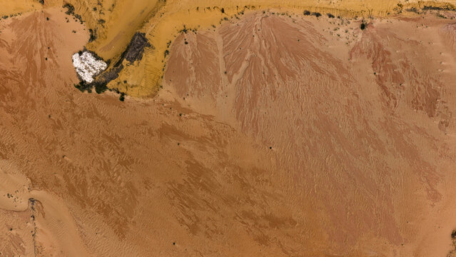 Aerial view of the textured landscape near Useless Loop, featuring intricate patterns of sand and salt deposits in shades of yellow and brown in Kalbarri, Western Australia, Australia.