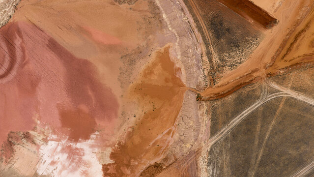 Aerial view of industrial salt mining patterns and salt lakes with vibrant pink, blue, and green hues contrasting with brown and yellow sand deposits in Kalbarri, Western Australia, Australia.