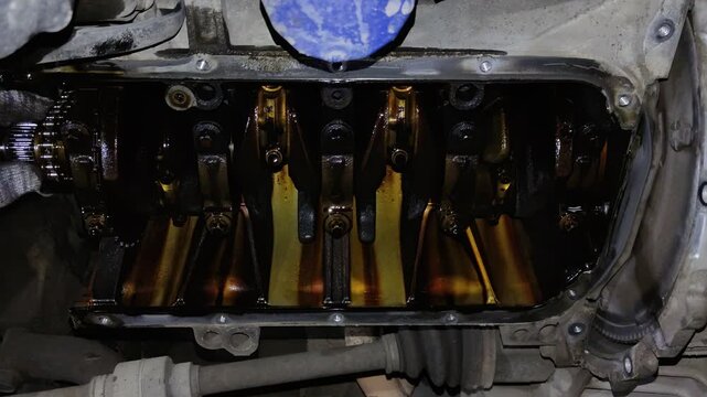 Under-car view of an open engine crankcase showing the oily crankshaft, counterweights, connecting rod caps, and internal mechanical components.