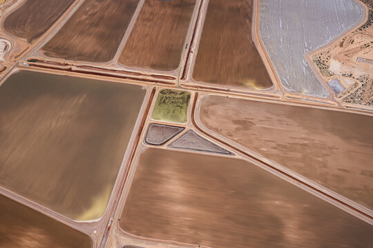 Aerial view of industrial salt mining ponds with geometric patterns, varying shades of brown and grey mineral-rich water, and earthen embankments in Kalbarri, Western Australia, Australia.
