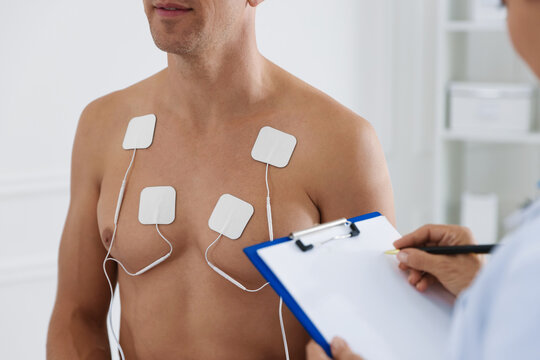 Doctor writing notes during patient's ECG test in clinic, closeup