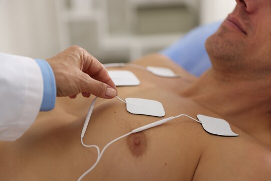 Doctor attaching ECG electrodes to patient's chest in clinic, closeup